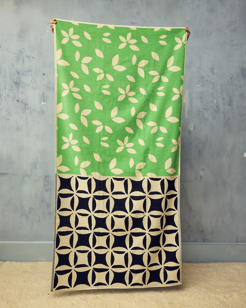 Green and black patterned beach towel against a gray wall.