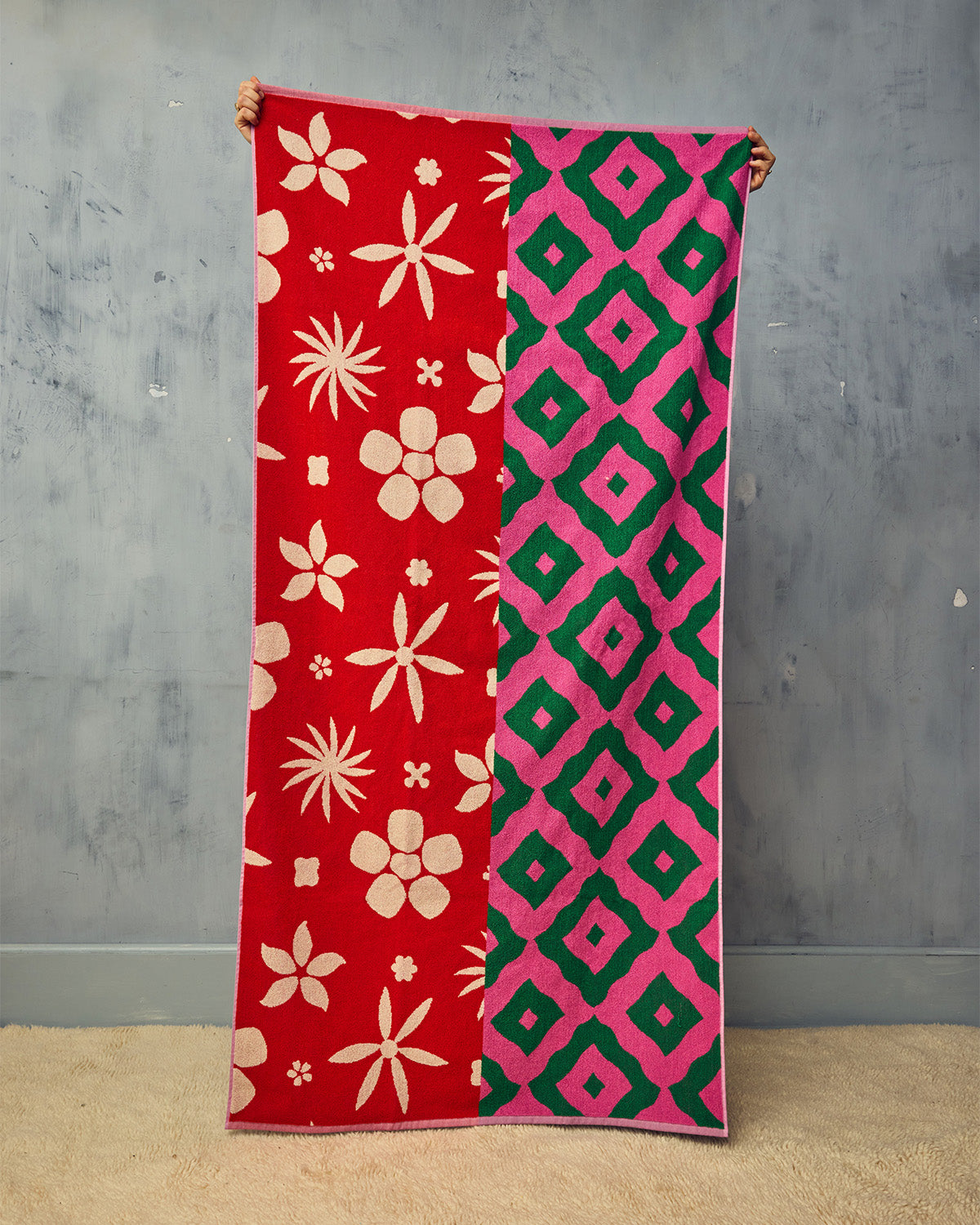 Peony towel being held up in front of plain plaster wall