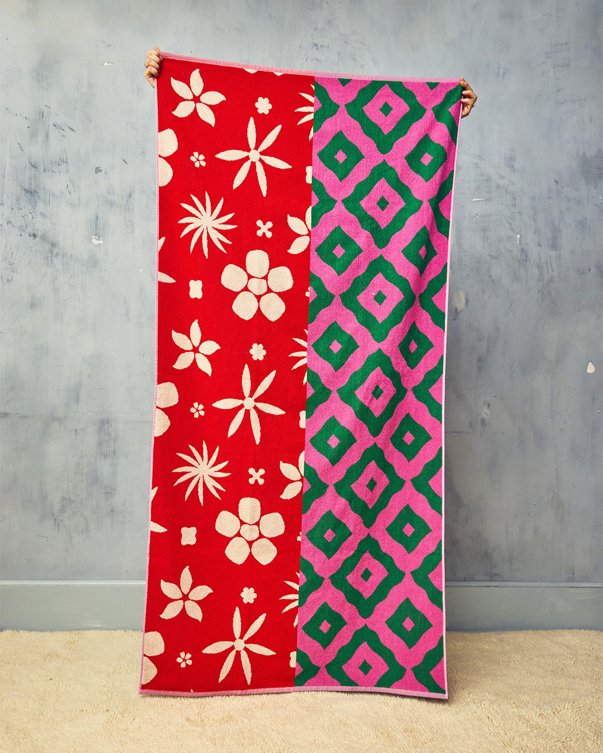 Patterned towel, half red with floral design and the other half green with pink geometric design, held against a gray wall.