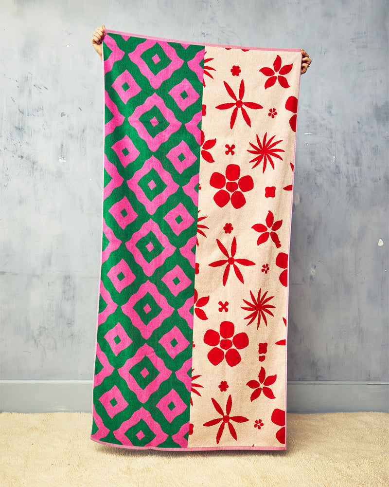 A patterned towel, one half green and pink geometric, the other red and beige floral, held against a gray wall.
