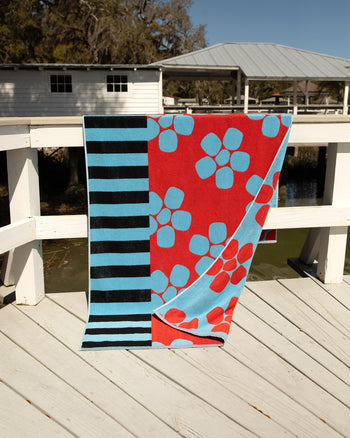 Periwinkle towel with different patterns on a wooden deck by a body of water. 