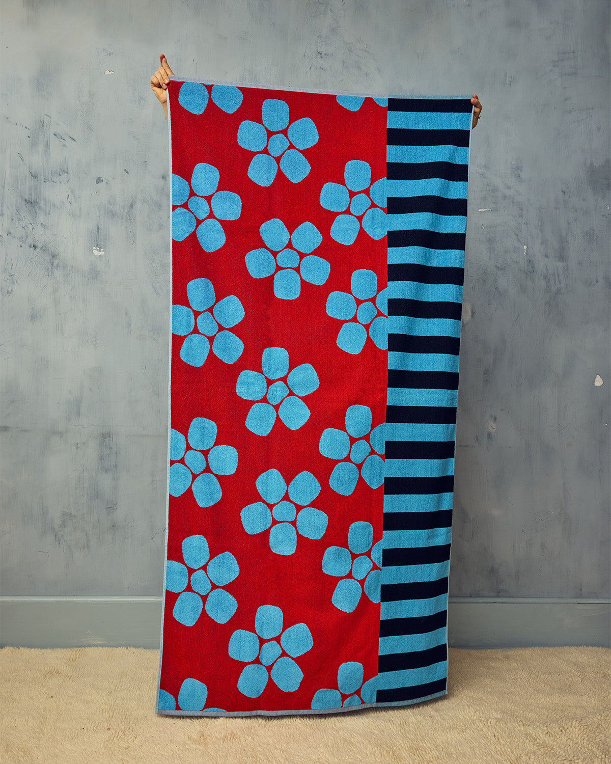 Towel with red background and blue floral pattern, held against a gray wall.