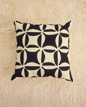 ["A square throw pillow with a black and cream geometric pattern, displayed on a textured beige rug.", " I like to think all these squares are stretching out to hold hands"]