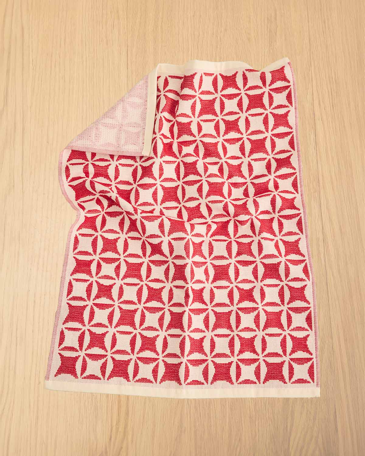 A folded red and cream geometric patterned knit blanket or throw laid flat on a light wood surface.