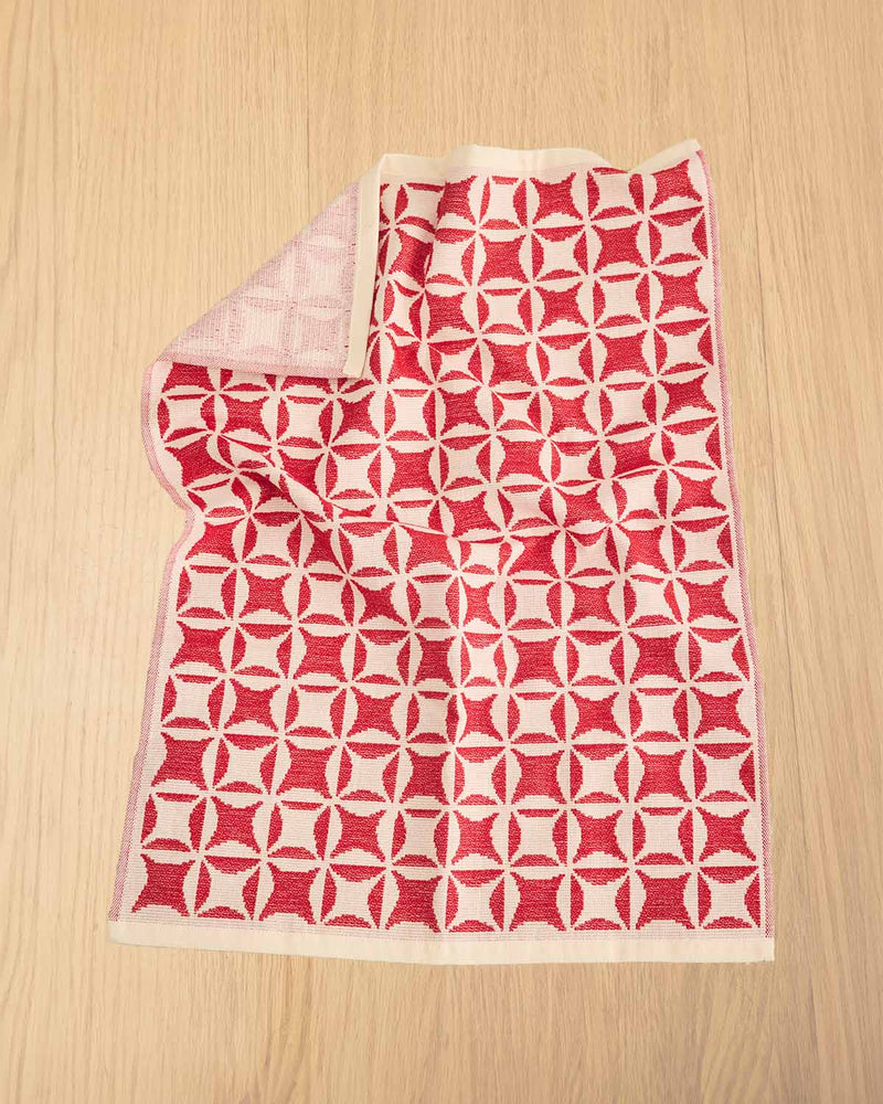 A folded red and cream geometric patterned knit blanket or throw laid flat on a light wood surface.