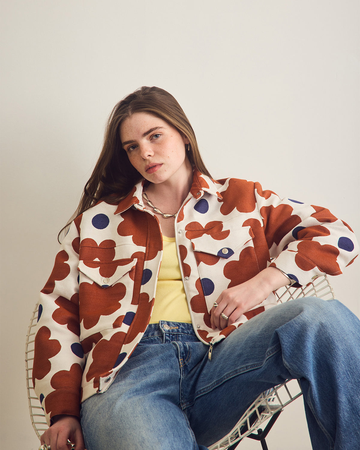 Woman wearing a patterned jacket sitting on a chair against a plain background