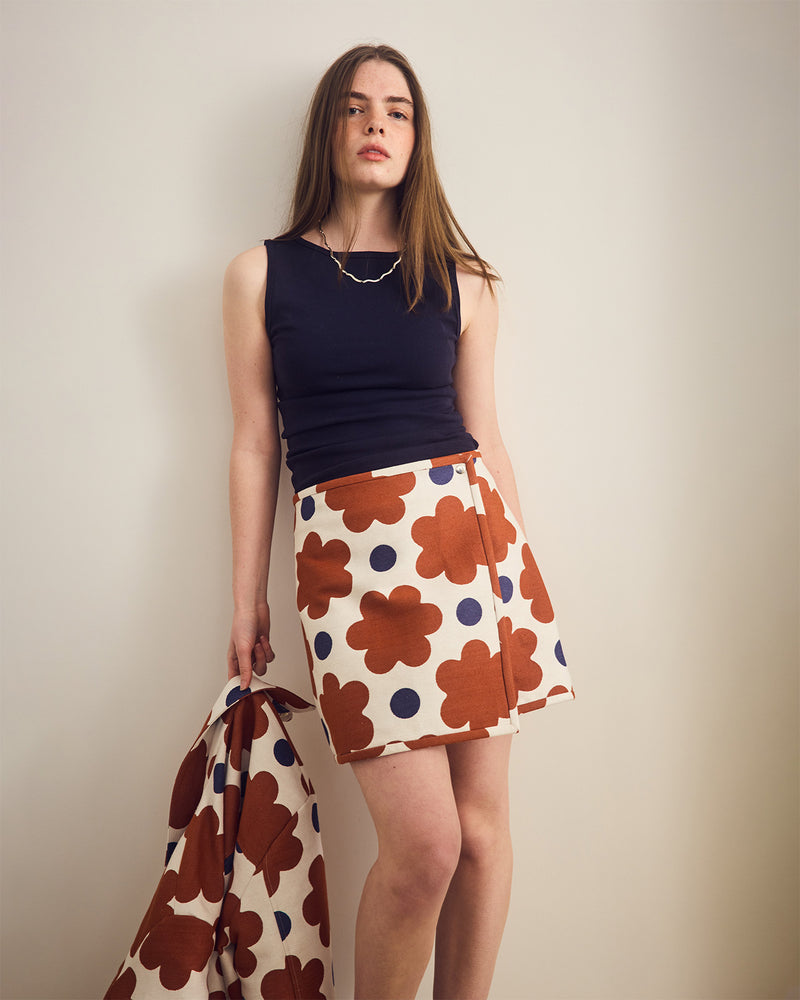 Woman wearing a navy top and floral skirt against a plain background