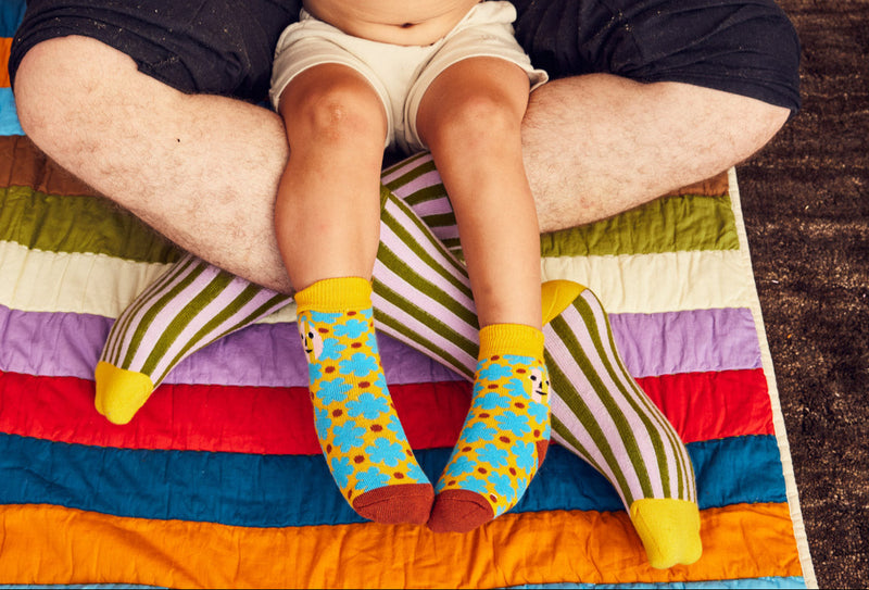 Child wearing colorful socks sitting on a person's lap with a multicolored blanket underneath.