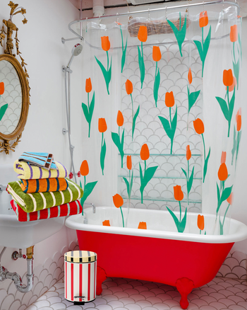 ["Bathroom with a red bathtub, floral shower curtain, and colorful towels. ", " People will ask if your bathroom got surgery, but it's really just a new outfit"]