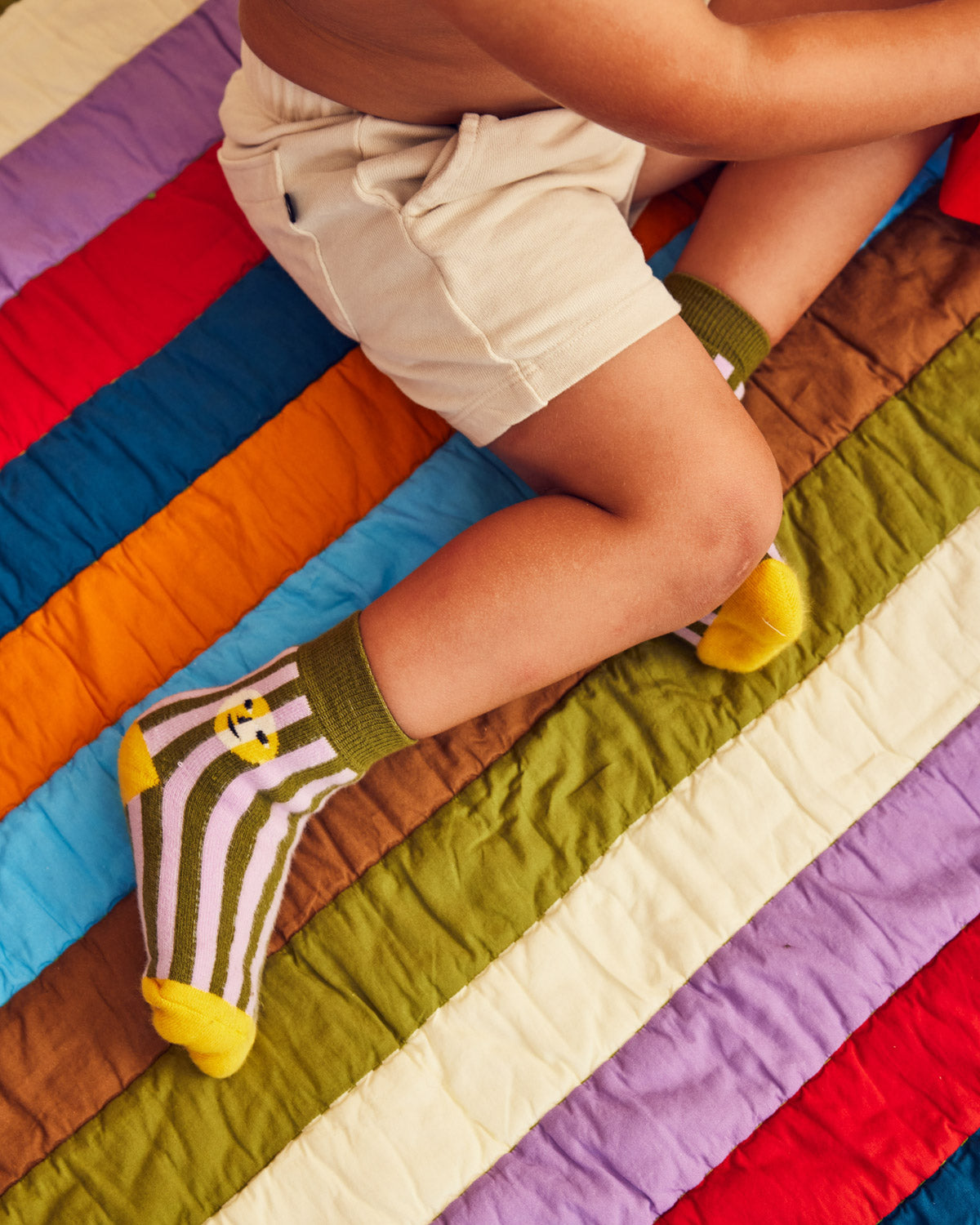 pair of sea stripe socks on child model's foot on a colorful quilt