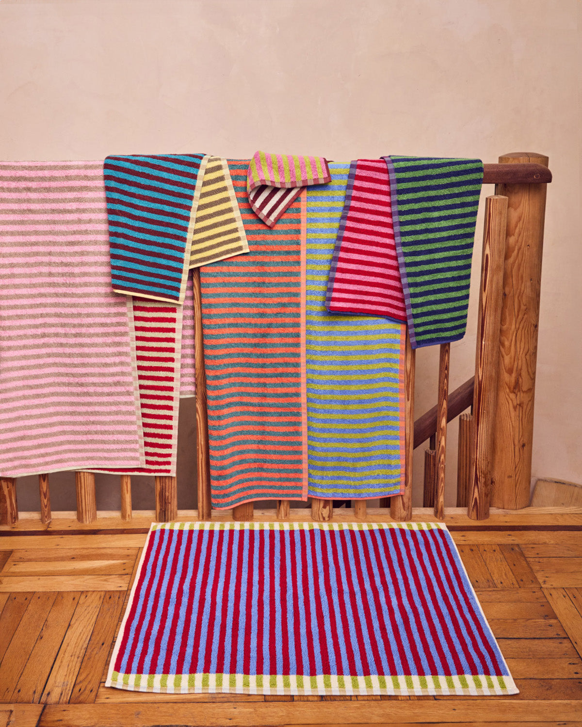 Colorful striped towels hanging on a wooden railing with a matching rug on the floor.