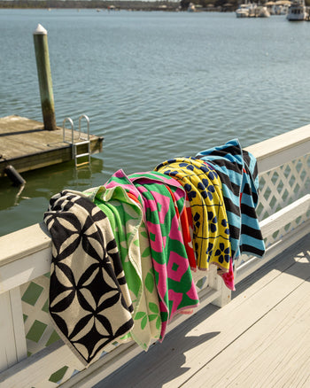 ["Colorful patterned blankets draped over a railing by a body of water with boats. ", " A towel for you, your two best friends, and one very special seagull."]
