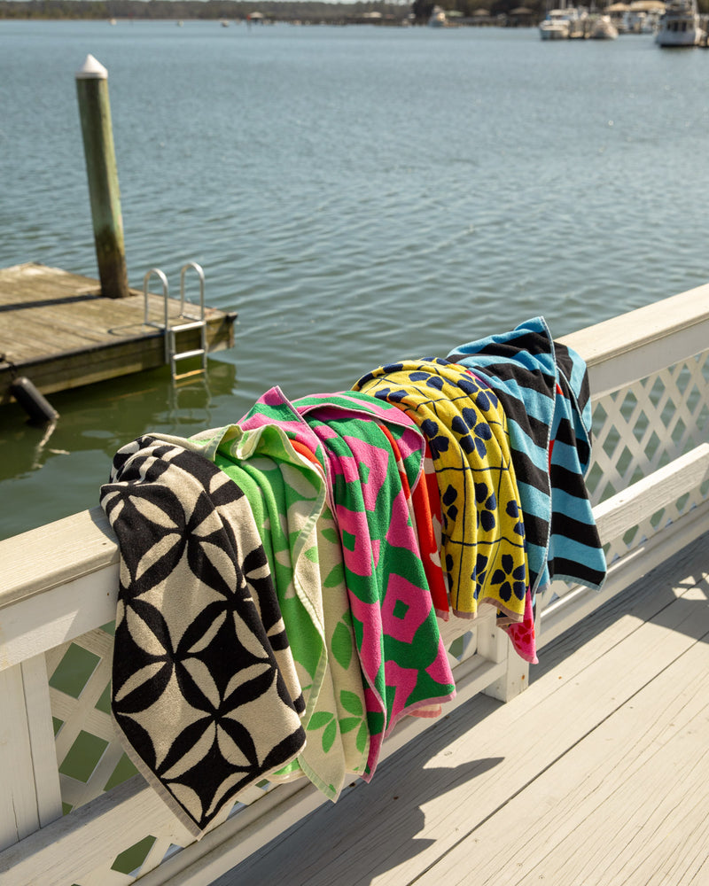 ["Colorful patterned blankets draped over a railing by a body of water with boats. ", " A towel for you, your two best friends, and one very special seagull."]