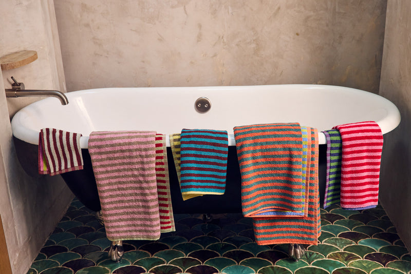 Colorful striped towels hanging over a white bathtub in a bathroom.