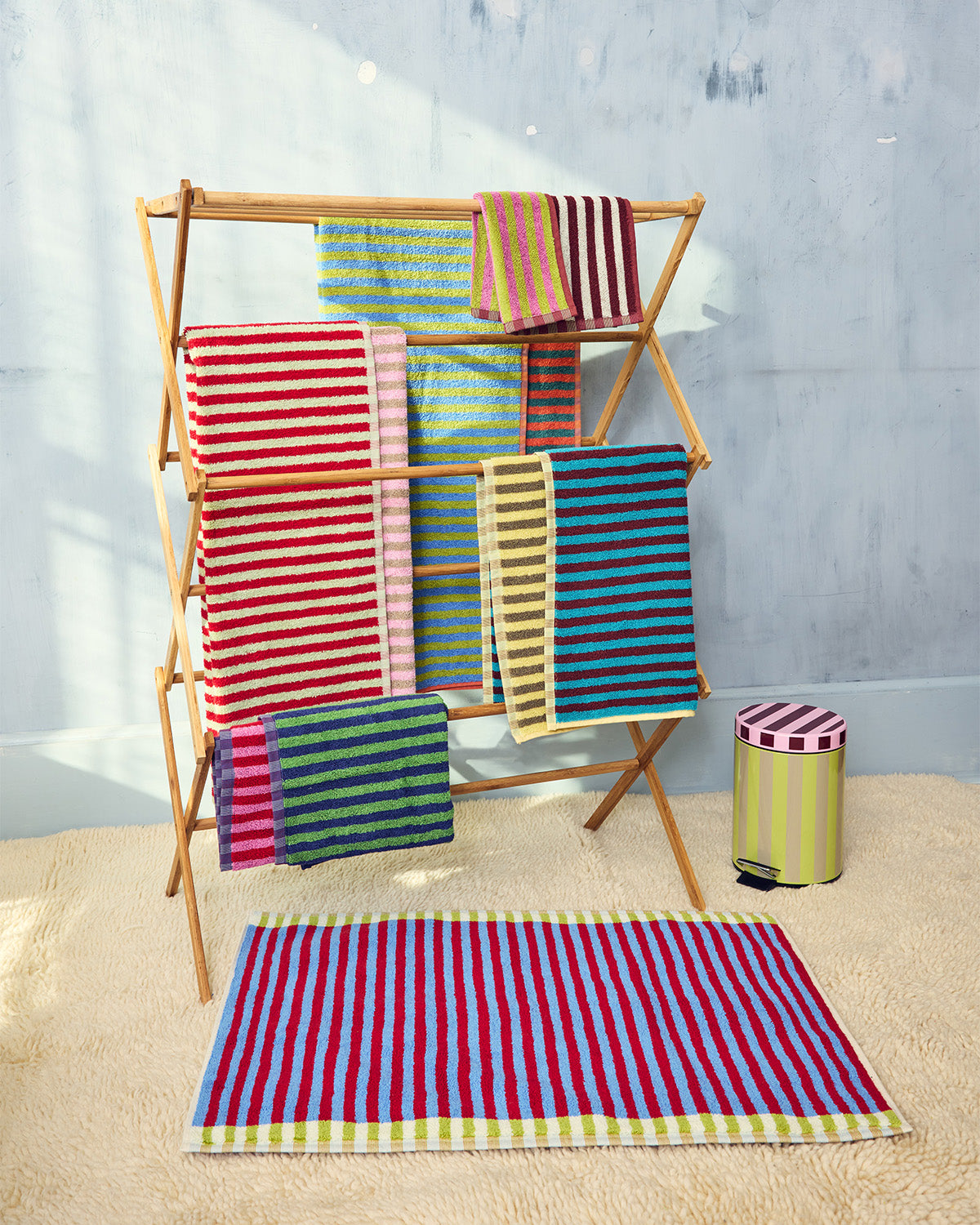 Colorful striped towels on a wooden rack against a light gray wall. 