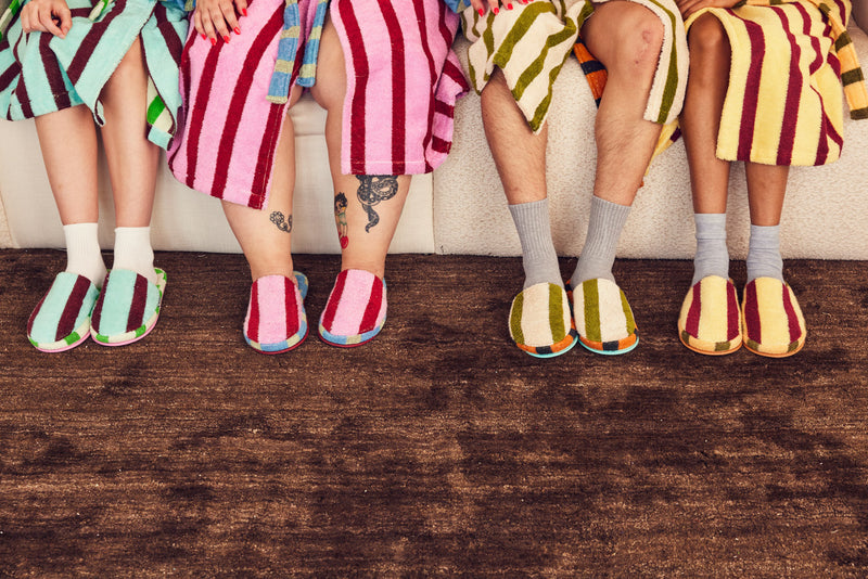 Four people sitting on a couch wearing colorful slippers and socks.