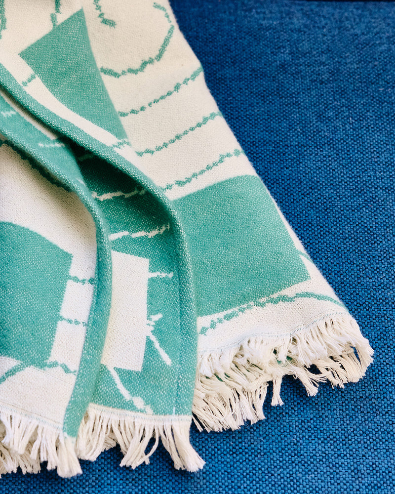 Teal and white patterned cotton throw with fringes on a blue background