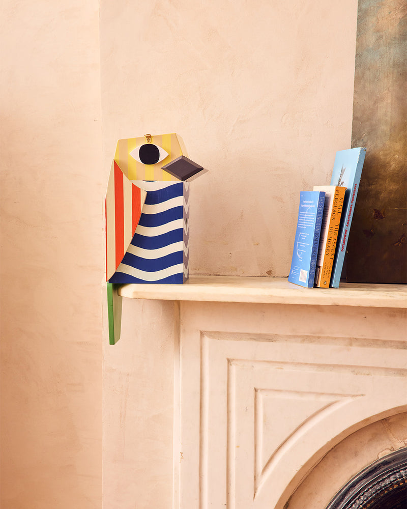 Decorative bird-shaped object on a shelf with books in the background
