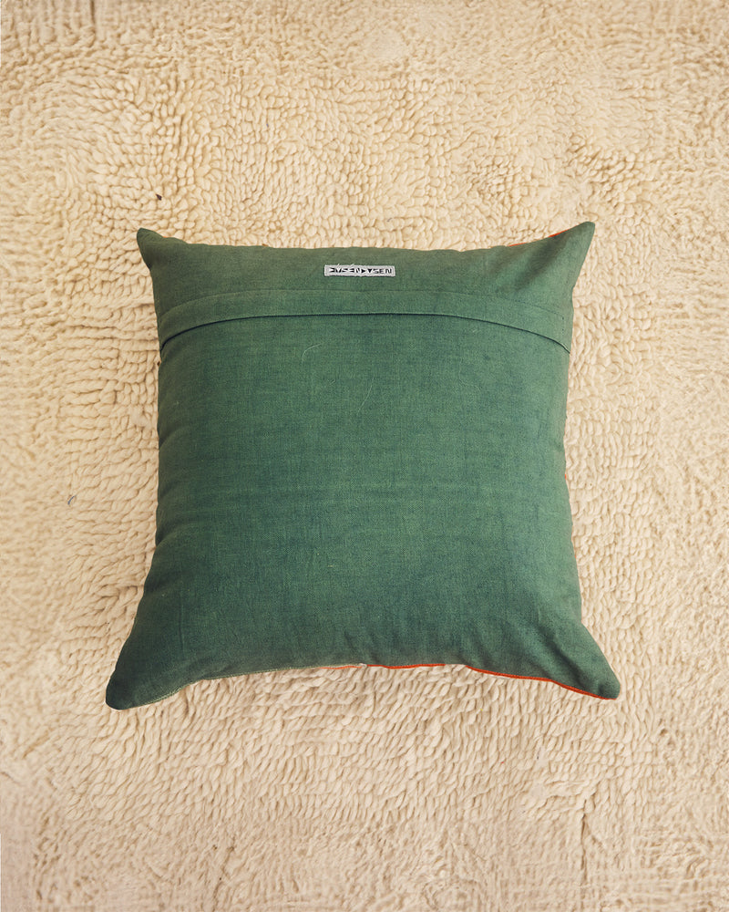 A square sage green throw pillow with a stitched horizontal seam across the middle , displayed on a textured beige rug.