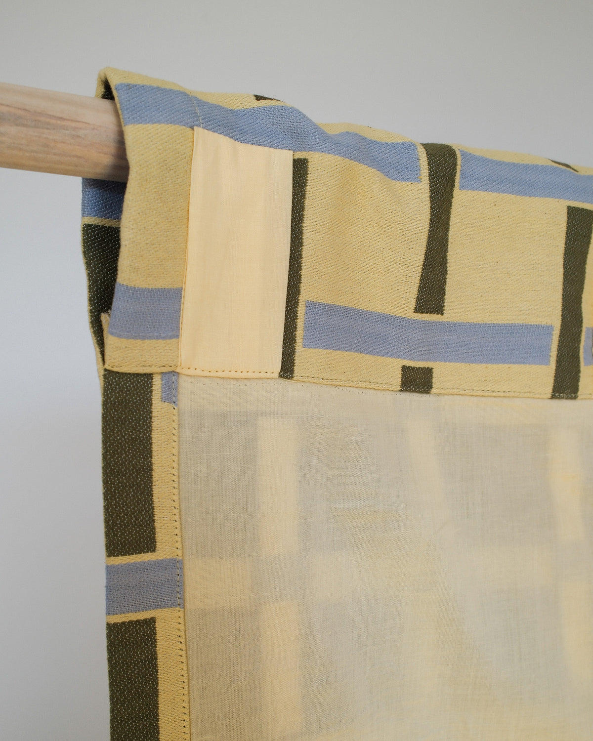 Textile with geometric pattern on a wooden rod against a gray background