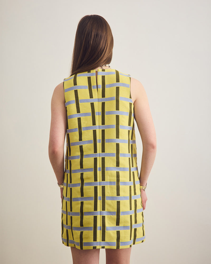 Woman wearing a sleeveless dress with a geometric pattern on a plain background