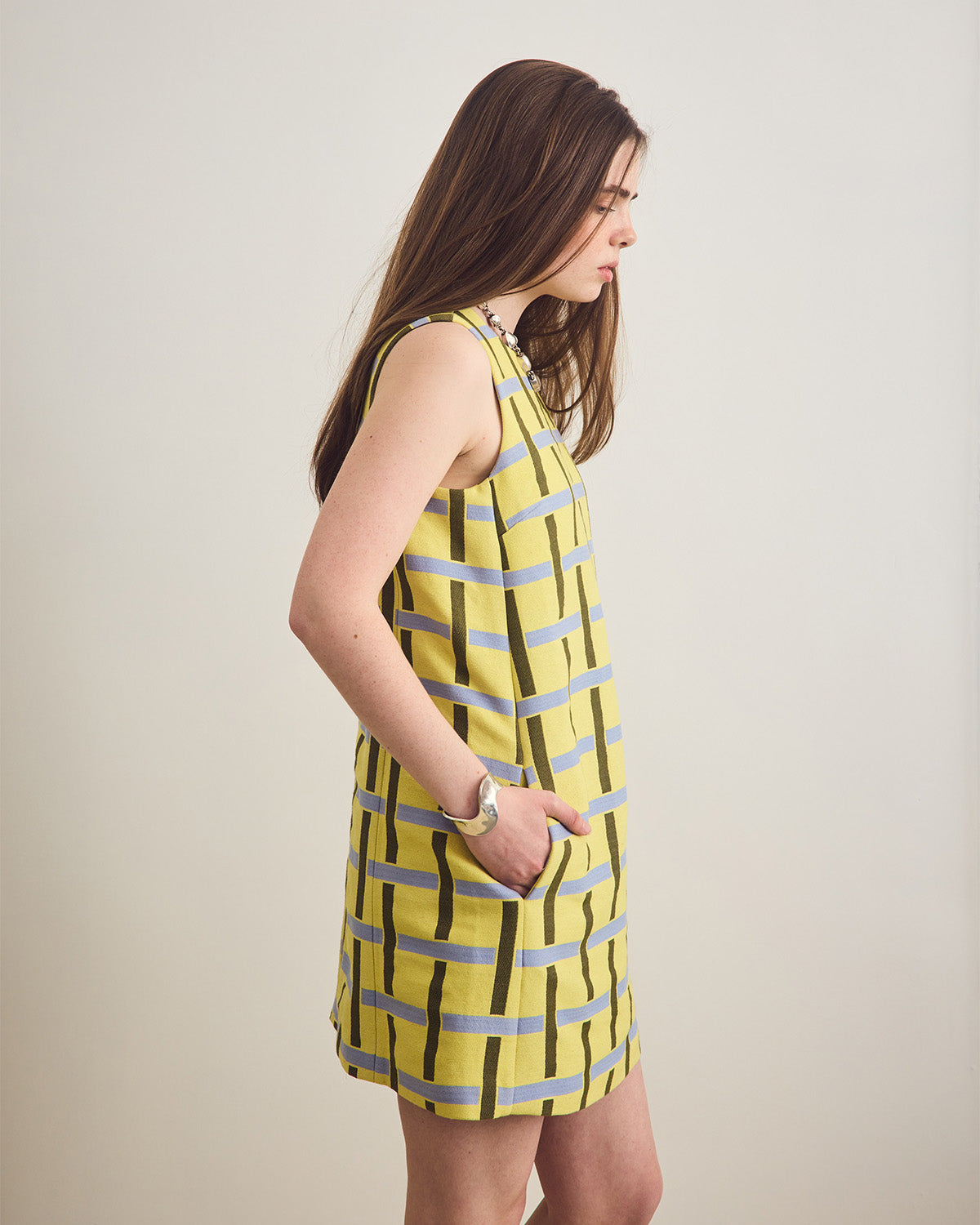 Woman wearing a yellow dress with green and blue stripes on a plain background