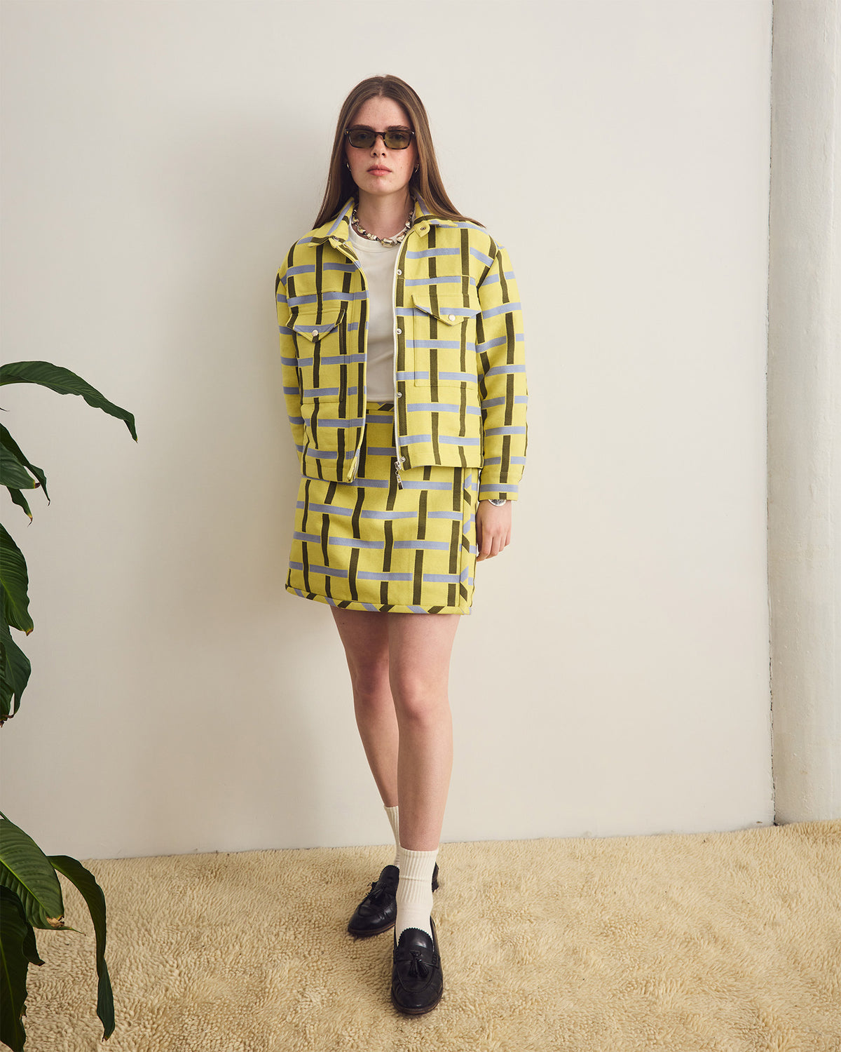 Woman wearing a yellow checkered outfit with sunglasses against a plain background