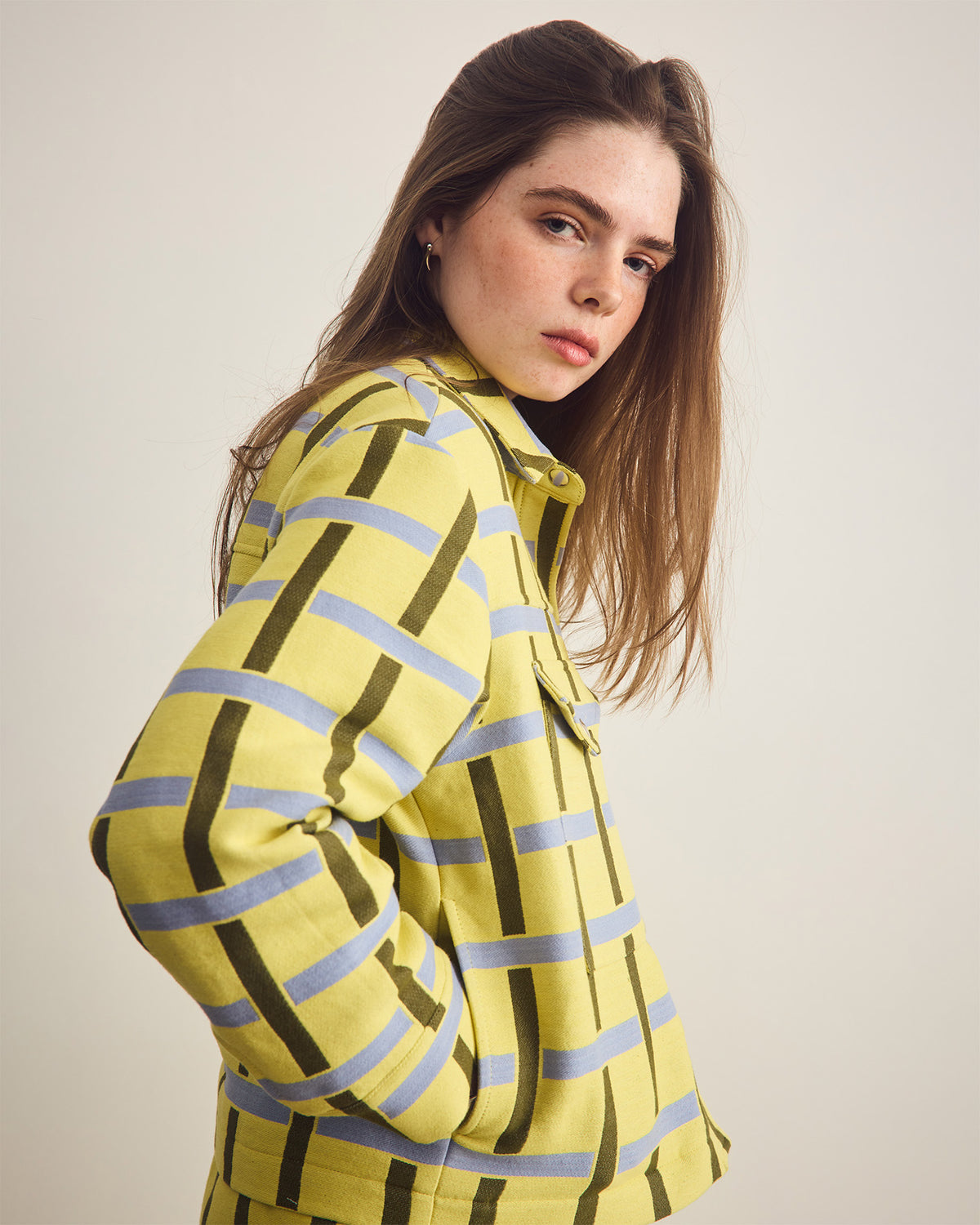 Woman wearing a yellow jacket with green and blue stripes on a plain background