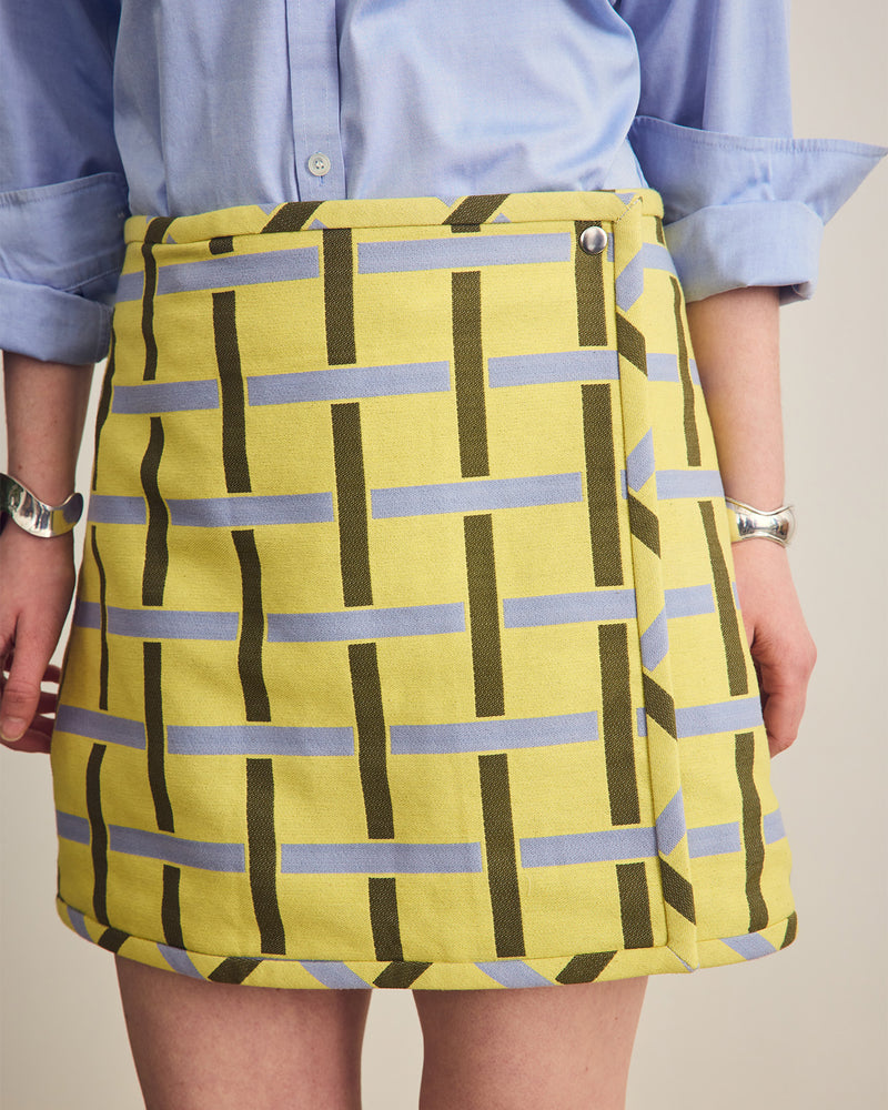 Person wearing a yellow skirt with blue and green pattern against a neutral background