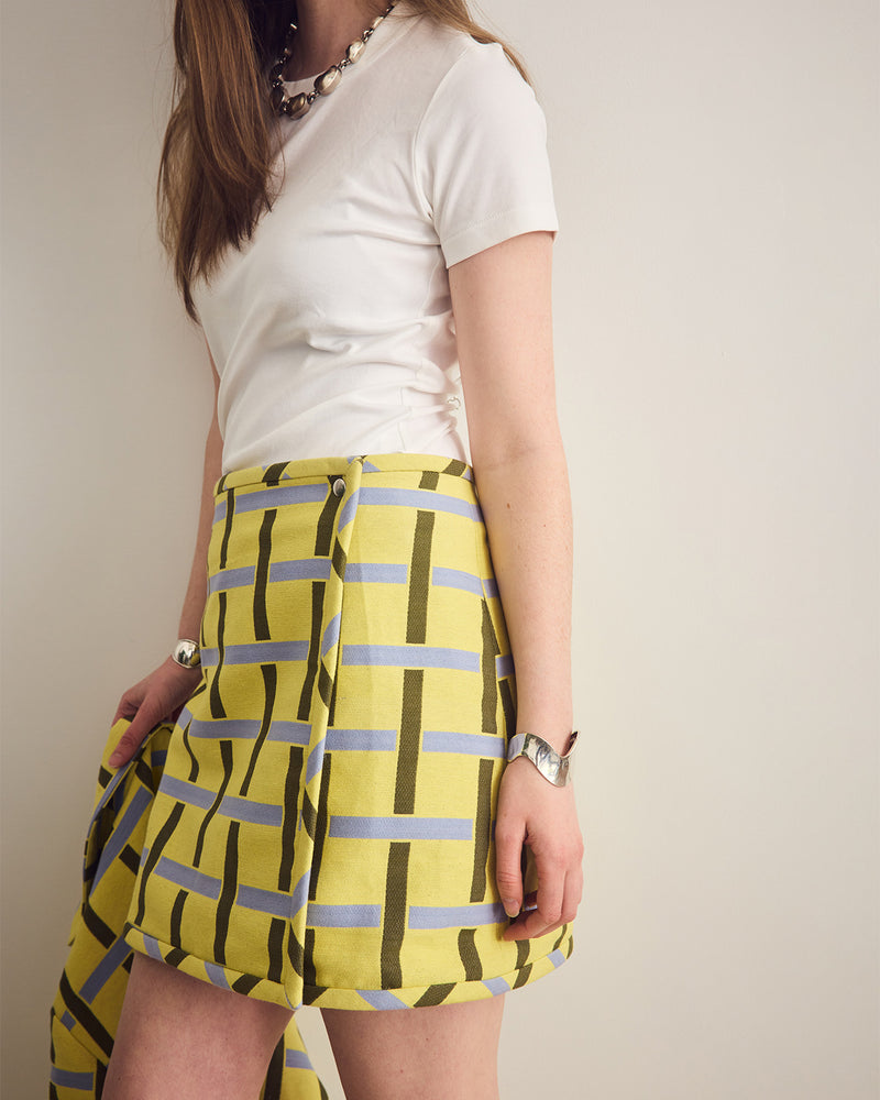 Person wearing a white top and yellow patterned skirt against a plain background