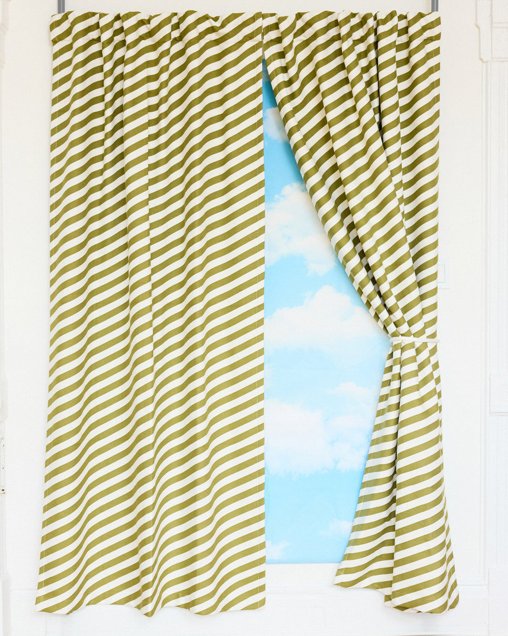 Green and white striped curtains with a clear blue sky and clouds on textile behind curtain