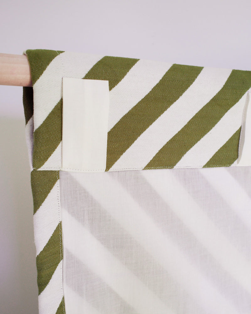 Fabric with green and white stripe pattern held by a hand against a light background