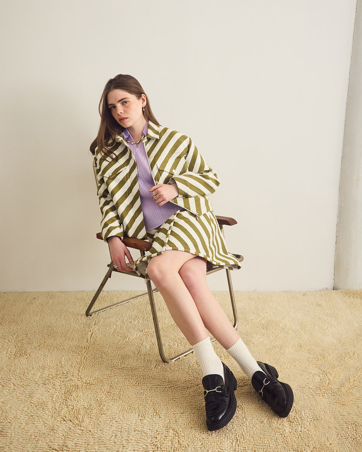 Woman in a green and white striped outfit sitting on a chair against a plain background