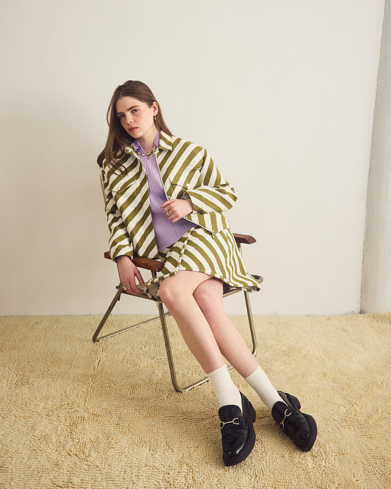Woman in a green and white striped outfit sitting on a chair against a plain background