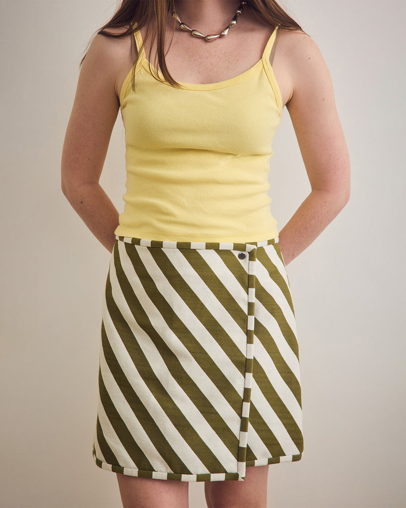 Woman wearing a yellow tank top and green and white striped skirt on a plain background