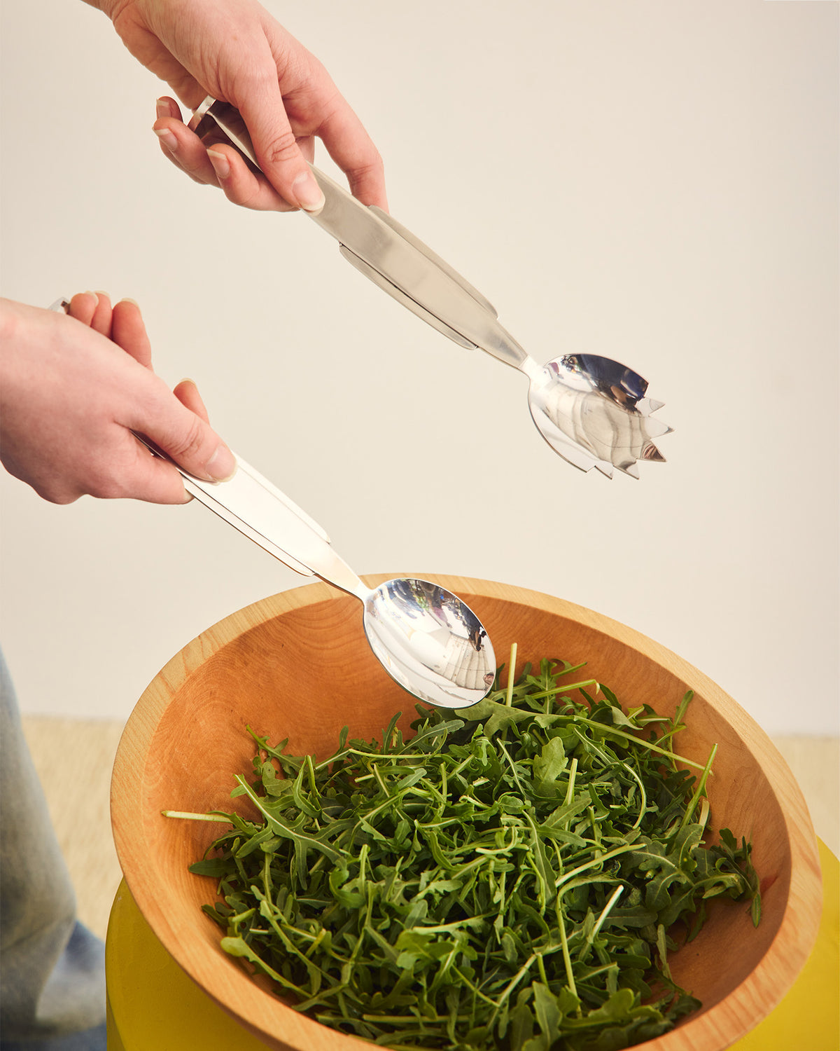 Wooden bowl with arugula and metal serving spoon and fork on a neutral background 