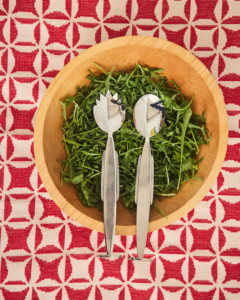 Wooden bowl with green salad and stainless steel salad servers on a red and white Quilt patterned tablecloth.