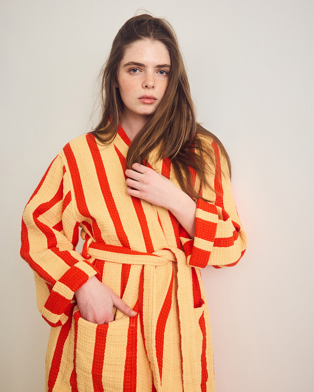 Woman wearing an orange-yellow and red striped robe against a plain background