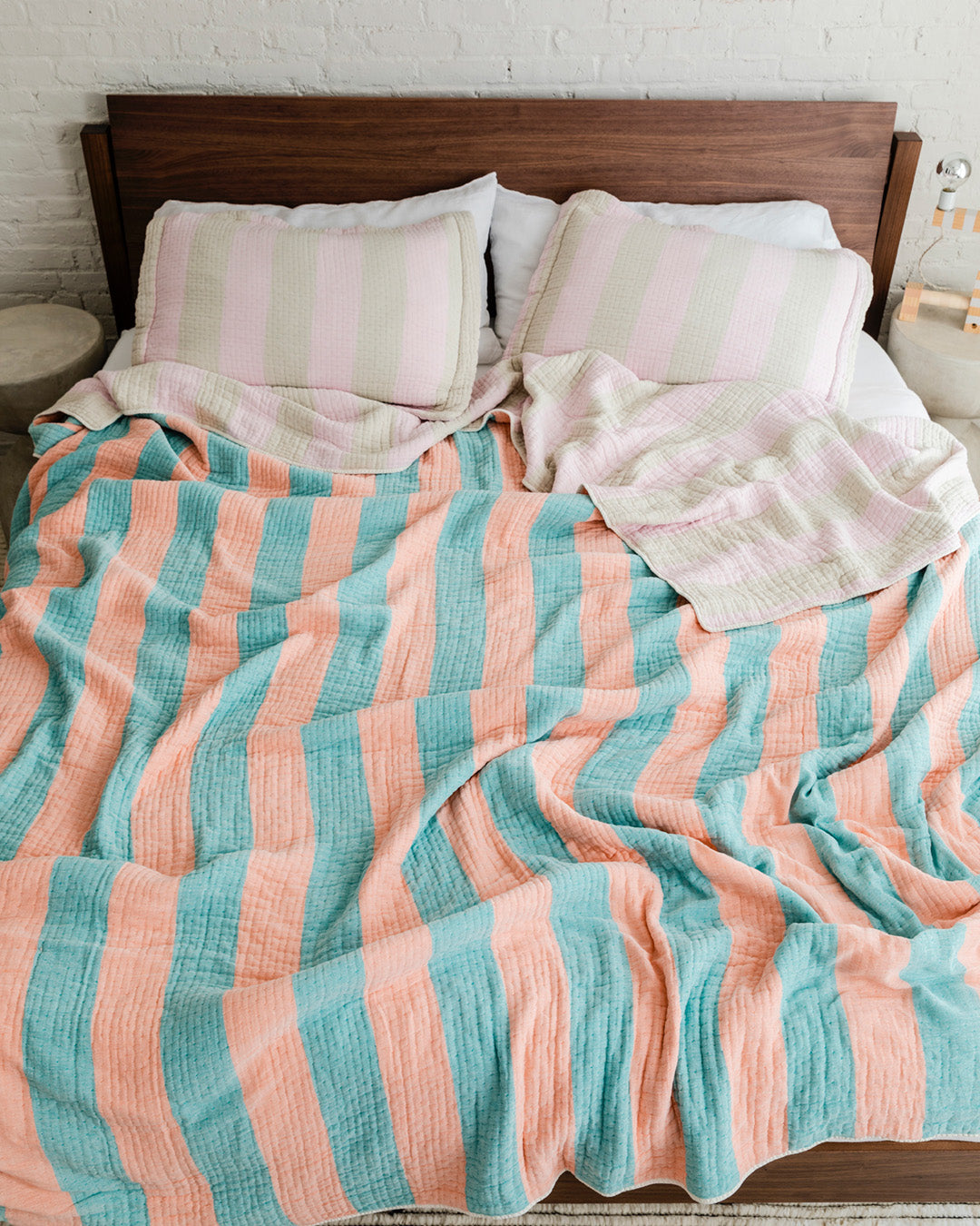 Dusen Dusen Warm Stripe Coverlet Set in reversible stripe colorways. Pink and beige stripes on one side, orange and green stripes on the other side. Woven matelassé coverlet with an inner layer of insulation for a quilted effect. Stonewashed, with an extra soft and gauzy hand feel. 100% cotton shell, polyester fill. Machine wash cold and tumble dry low. Made in Portugal