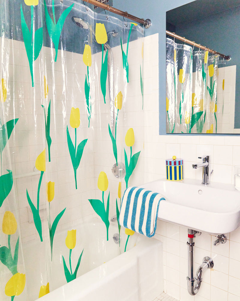 Dusen Dusen Tulip Shower Curtain. Yellow tulip petals with green stems printed on clear background. Embossed logo in bottom corner. 100% PEVA free of PVC and BPA. 12 anti-rust stainless steel grommets.