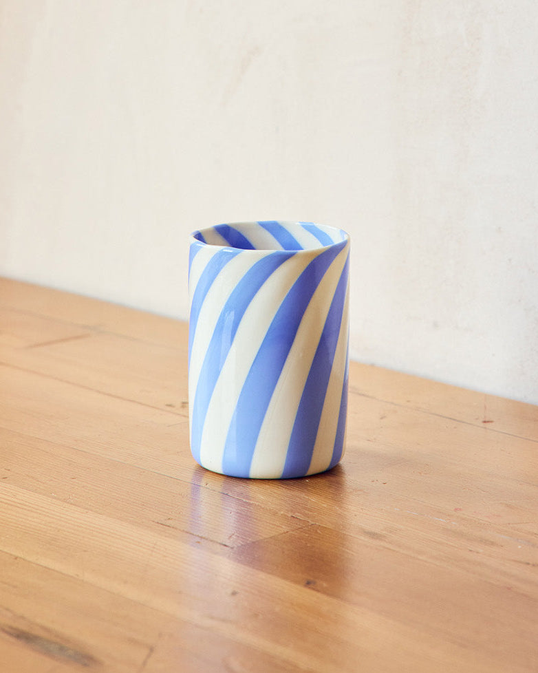 Blue and white striped  Murano glass on a wooden surface with a plain wall background