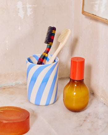 Bathroom counter with striped Murano glass cup, brushes, and a bottle on a light background