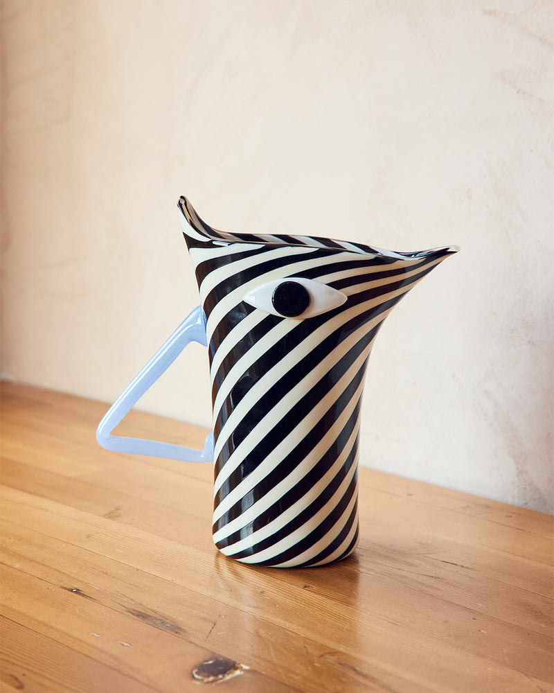 Black and white striped pitcher with a blue handle on a wooden surface