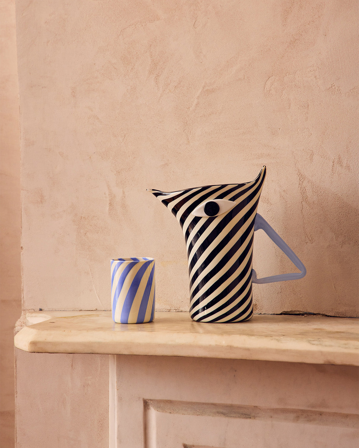 Striped Murano glass pitcher and cup on a wooden surface with a beige wall background shaped like a Zebra 
