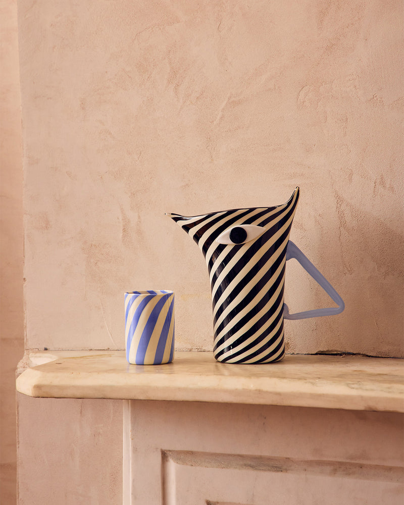 Striped Murano glass pitcher and cup on a wooden surface with a beige wall background shaped like a Zebra 