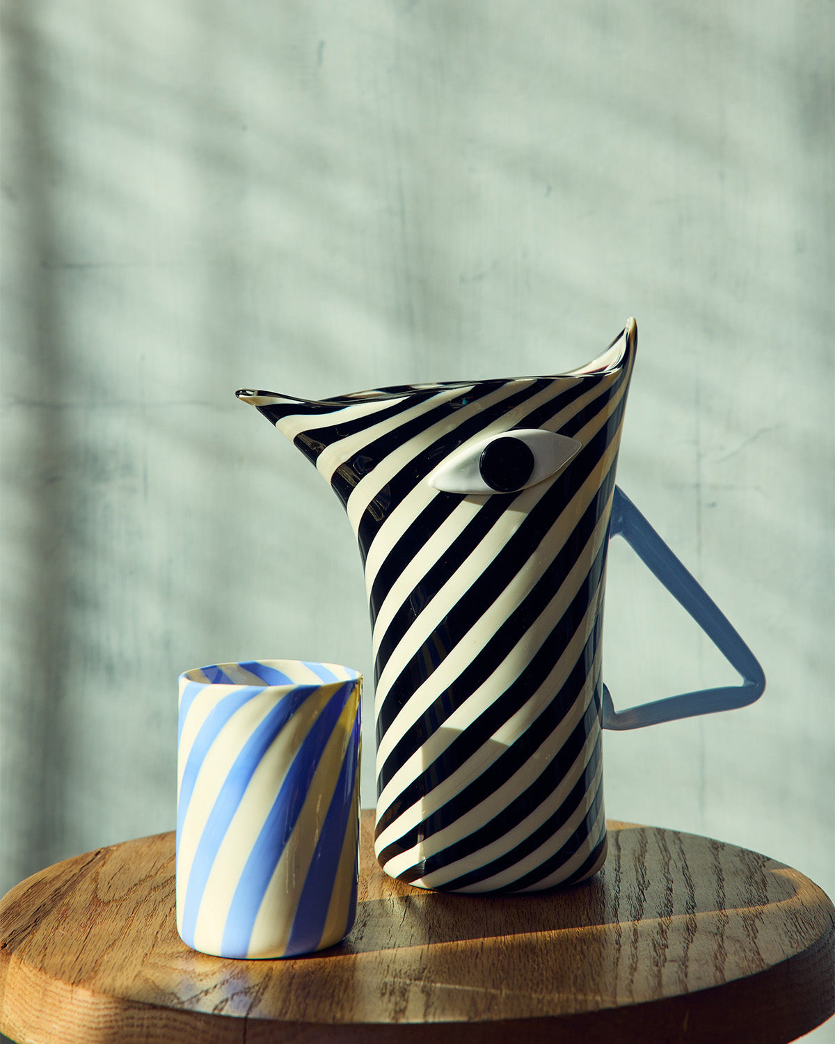 Black and white striped pitcher with a blue and white striped murano glass on a wooden surface.