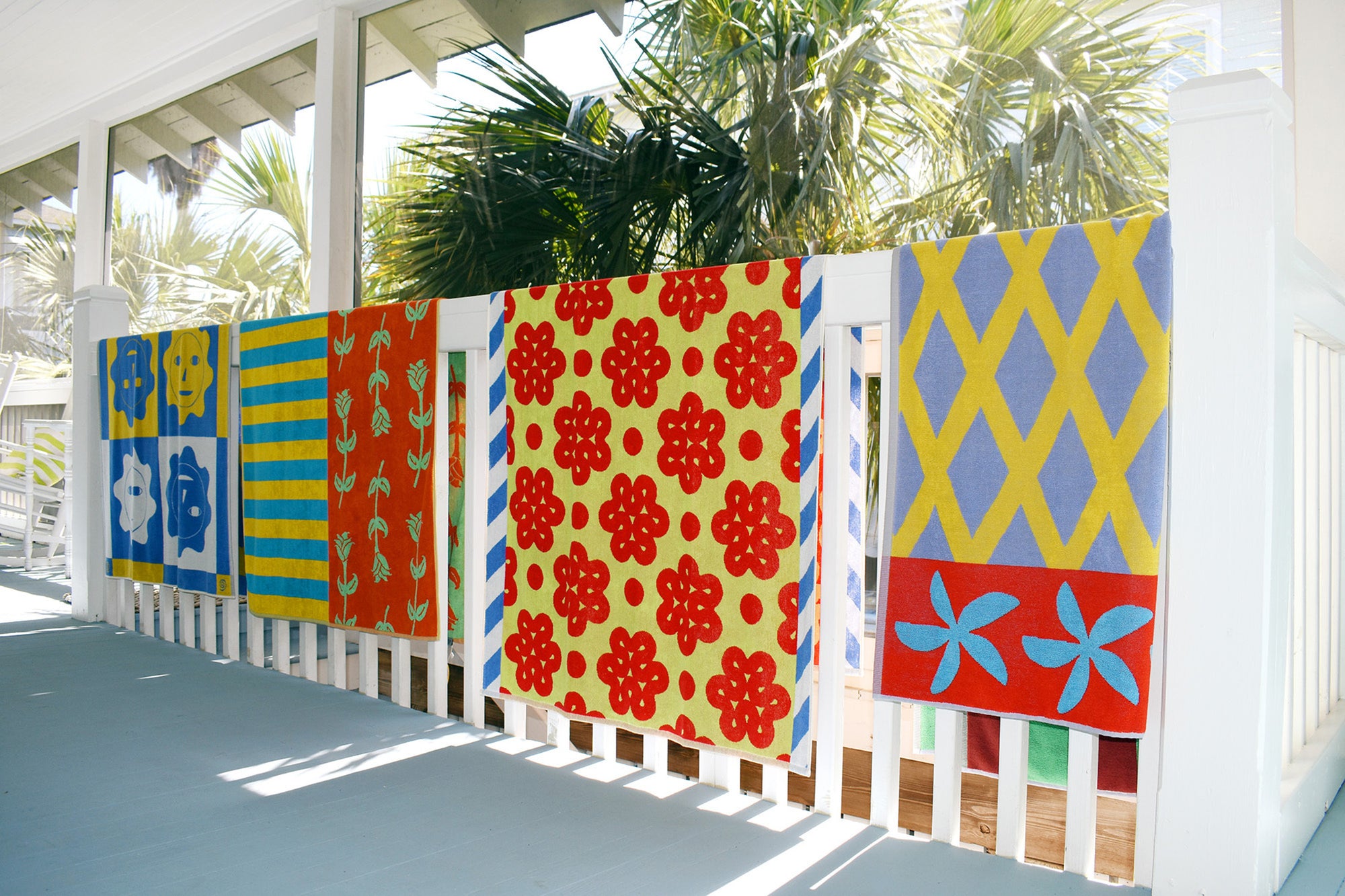 beach towels all on a railing with palms behind them