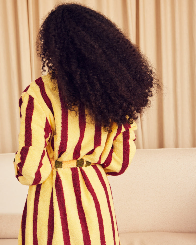 Person wearing a yellow and red striped robe from behind with beige curtains in the background