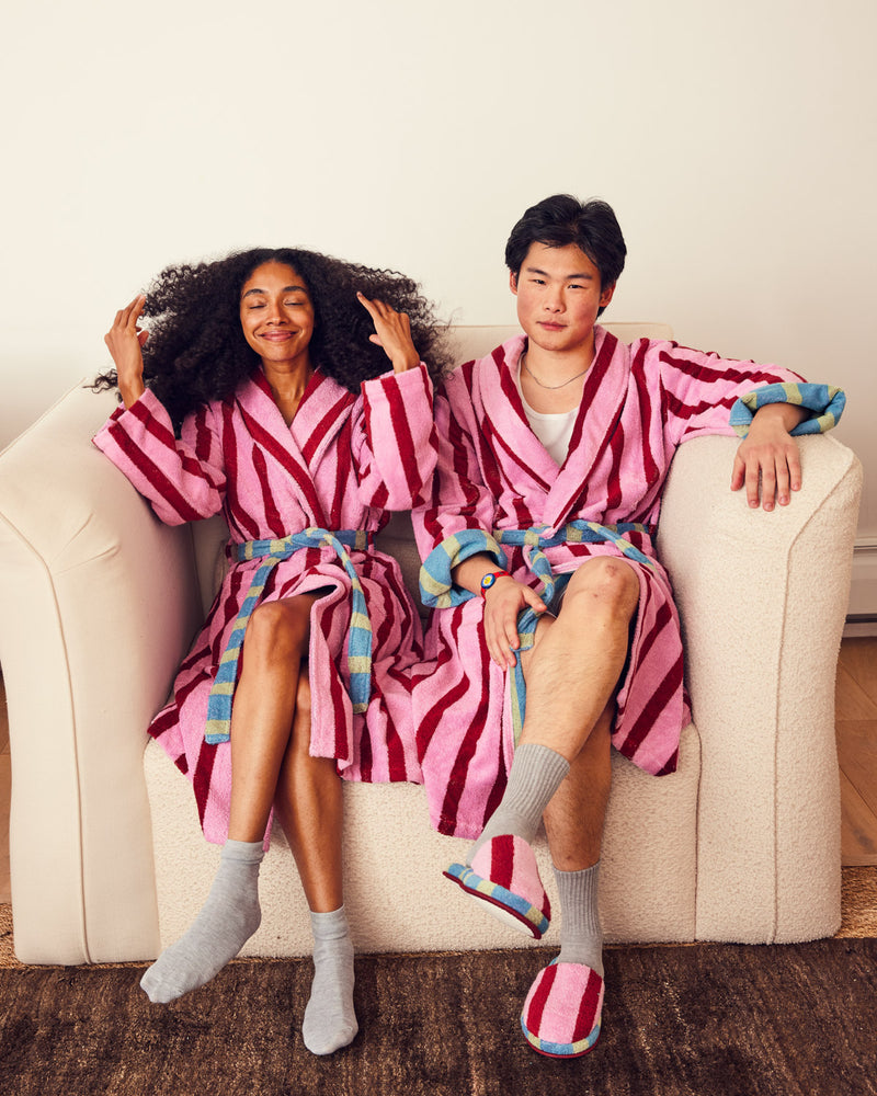 Two people sitting on a couch wearing matching pink and red striped robes.