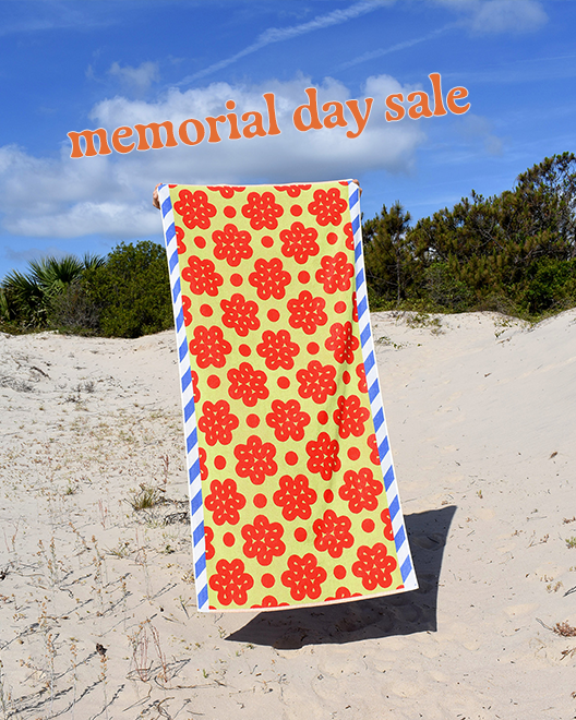 memorial day in orange text over Raspberry beach towel on beach